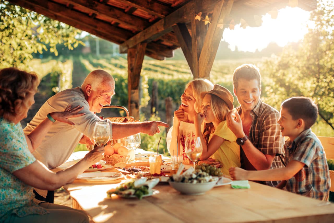 Photo of a multigenerational family gathered around an outdoor dinner table in the evening