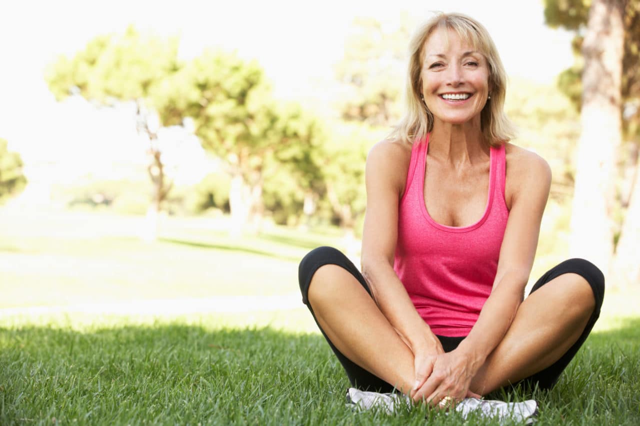 Photo of a smiling person in work-out gear sitting cross-legged on the grass