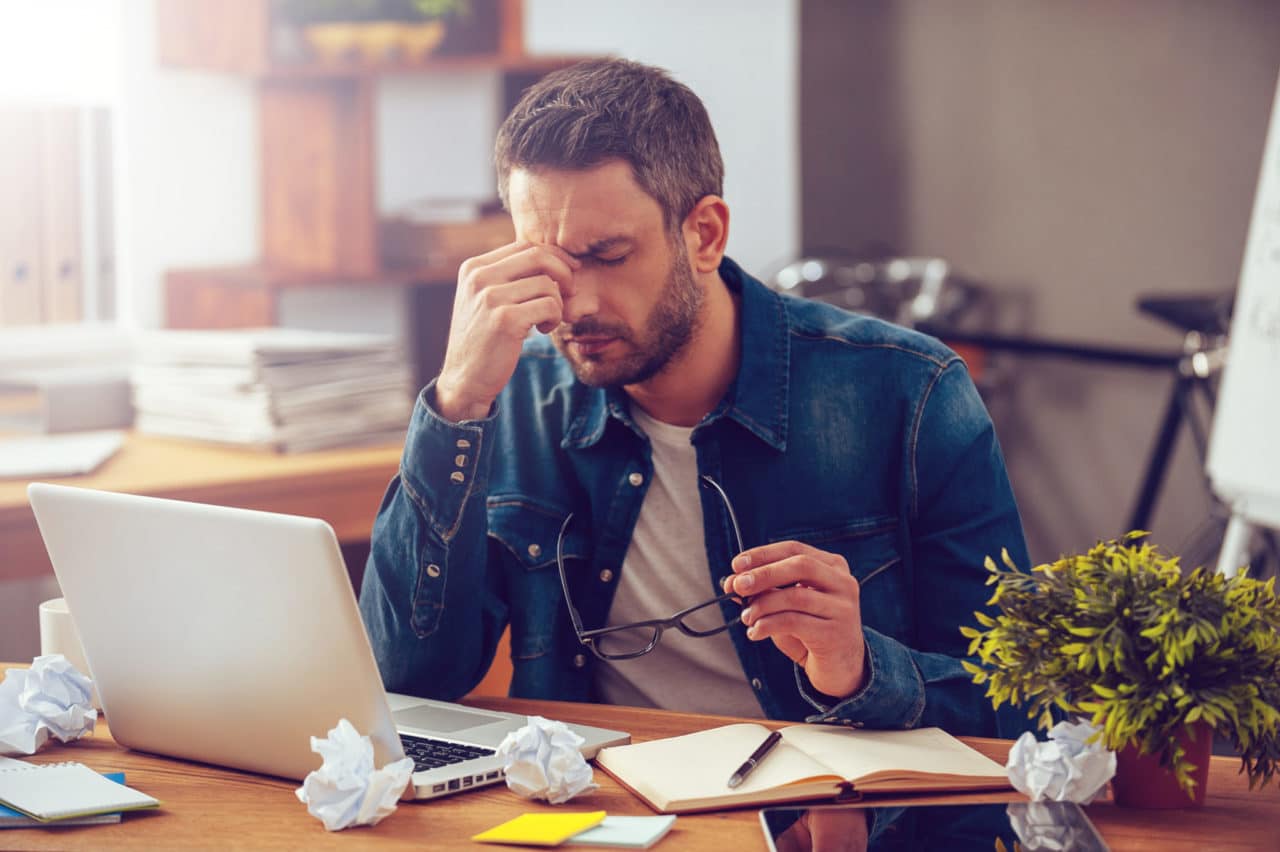 Photo of a person sitting at a desk and pinching the bridge of their nose in pain