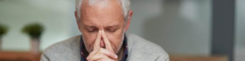 A person sitting on a bench, resting their head on their steepled index fingers and looking disappointed