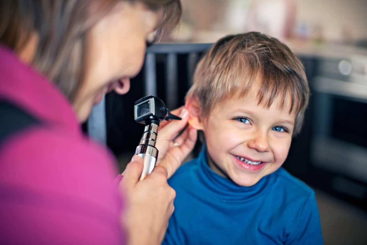 Child smiling as an audiologist holds an otoscope to their ear