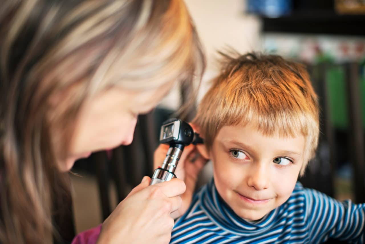 A child smiling up at the audiologist holding an otoscope to their ear
