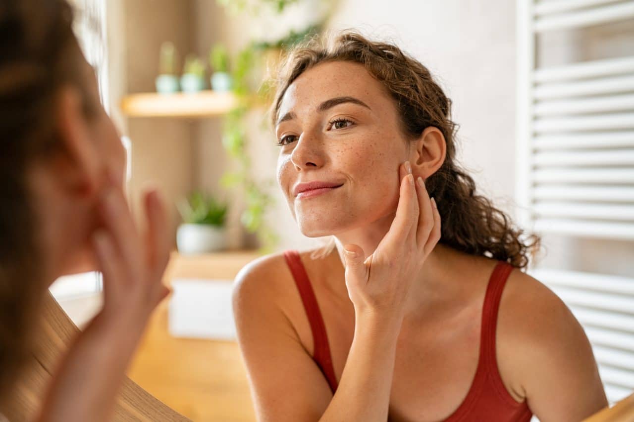Young woman looking at her face in the mirror.
