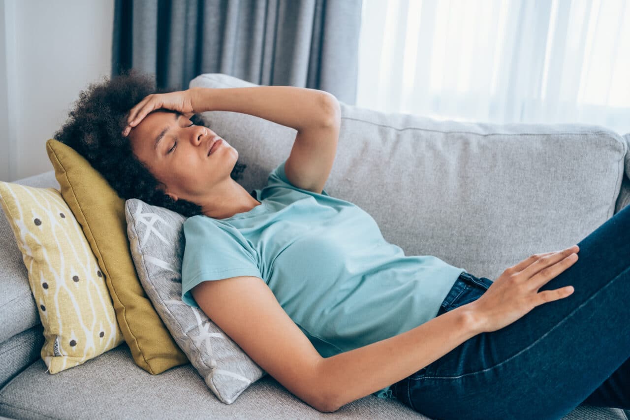 Sick young woman lying on the couch and holding her head with hand. Ill woman lying on the sofa