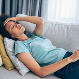 Sick young woman lying on the couch and holding her head with hand. Ill woman lying on the sofa