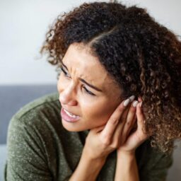 Woman experiencing ear pain, holding her hands to her ears.