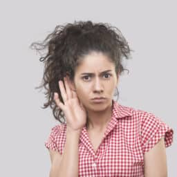 Young woman holding her hand to her ear looking confused