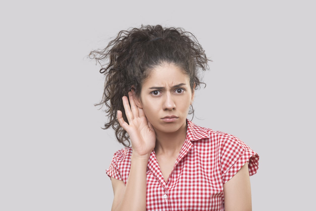 Young woman holding her hand to her ear looking confused.