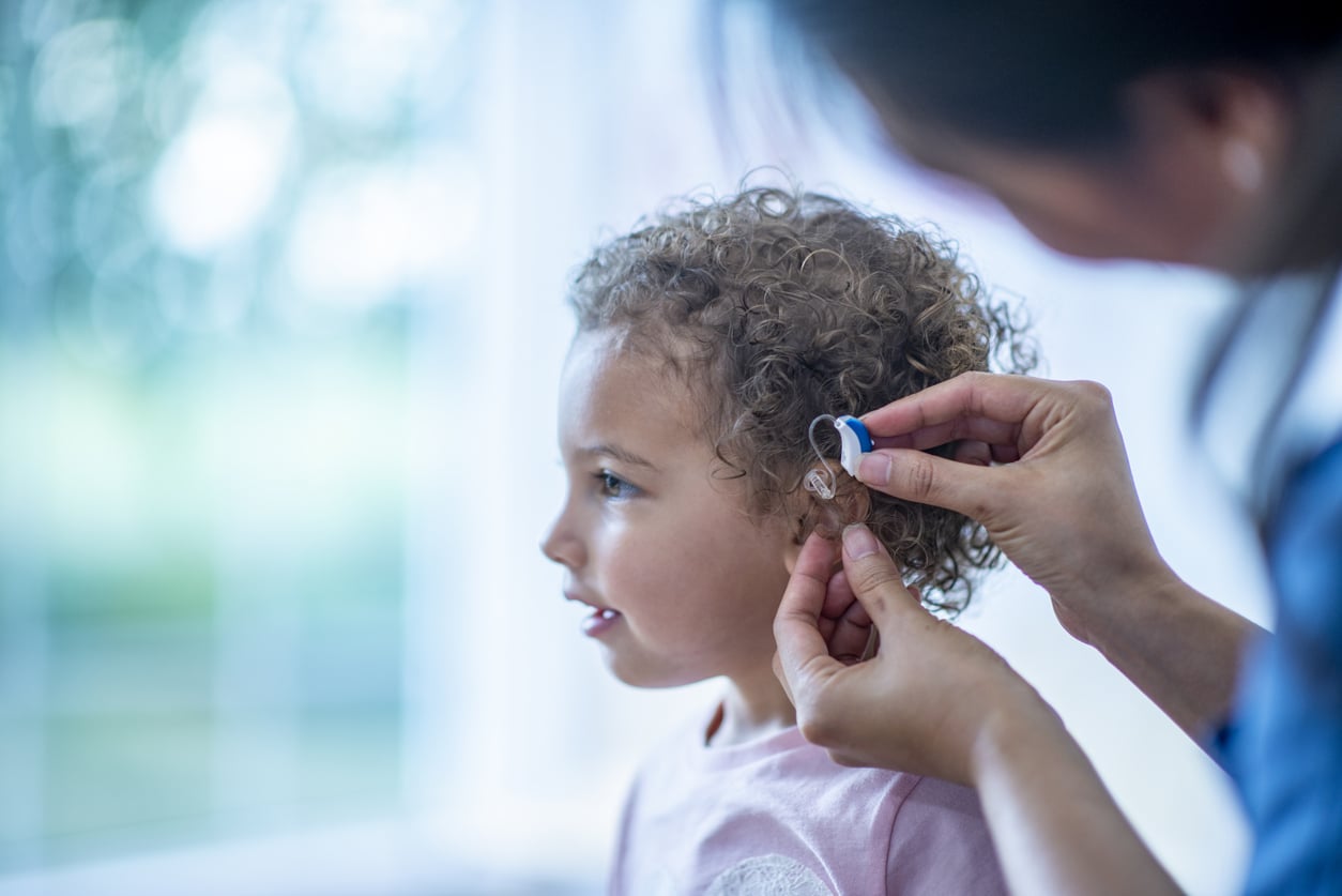 Provider putting a hearing aid in a young girl's ear.