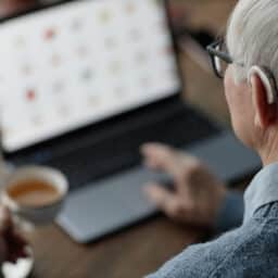 Senior Man Wearing Hearing Aid Working on Laptop at Home
