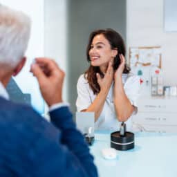 Audiologist showing hearing aid to senior patient in medical center