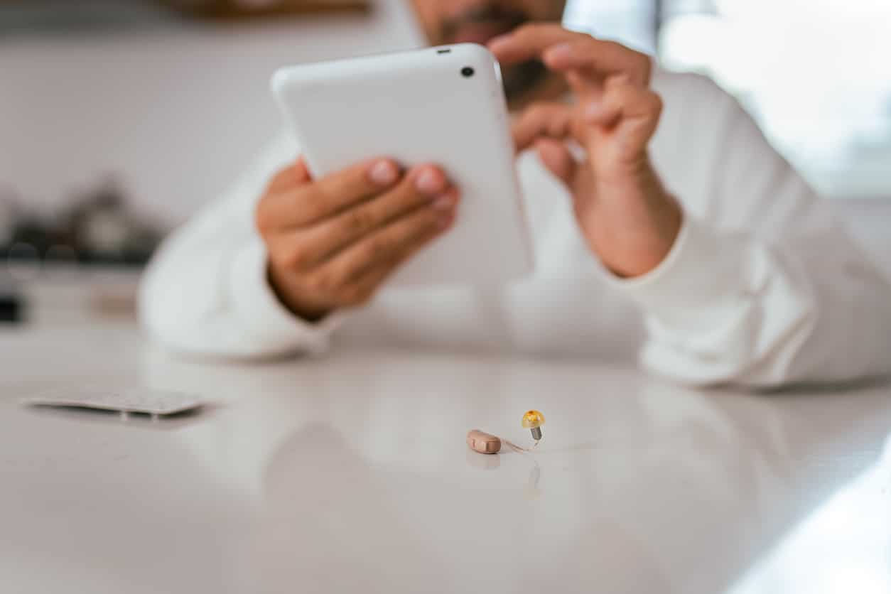 Modern hearing aid, man using a tablet in the background.