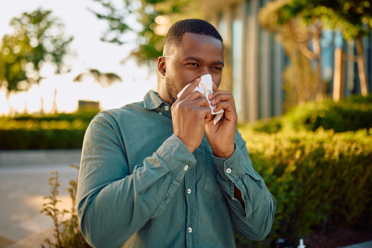 Man with allergies blowing his nose outdoors.