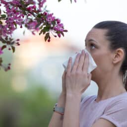 Woman blowing her nose standing by a flowering tree.