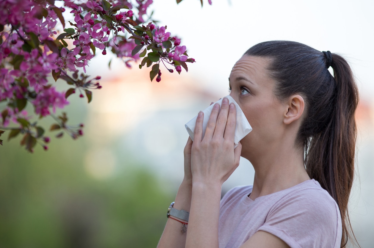 Woman blowing her nose standing by a flowering tree.