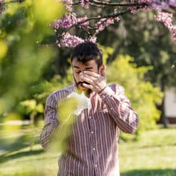 Man itching his eyes and blowing his nose in the park.