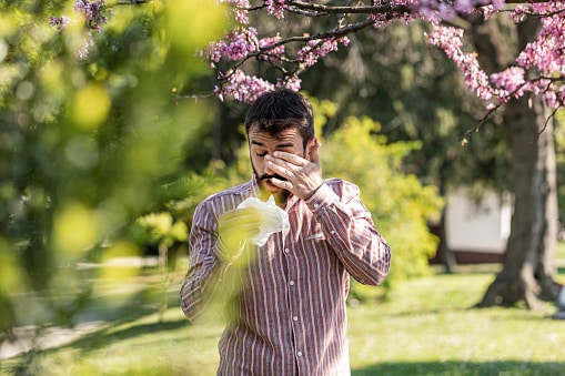 Man itching his eyes and blowing his nose in the park.