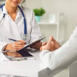 Doctor writing on her chart while talking to her patient.