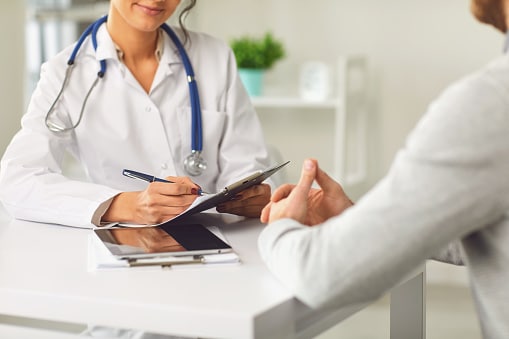 Doctor writing on her chart while talking to her patient.