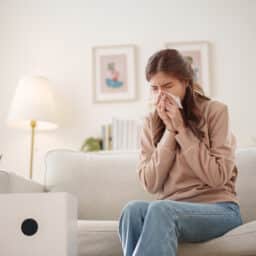 Woman sneezing and holding a tissue to her nose.