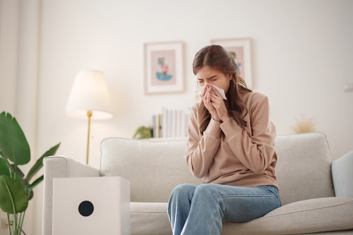 Woman sneezing and holding a tissue to her nose.