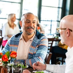 Two men having lunch at a restaurant. One is wearing a hearing aid.