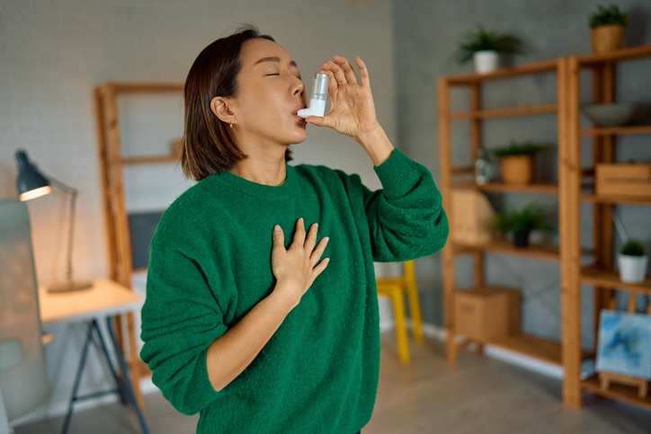 Woman at home reaching for an inhaler during an asthma attack.